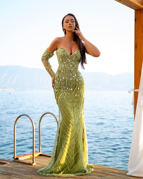 Woman in a green sequined dress standing on a dock with water in the background
