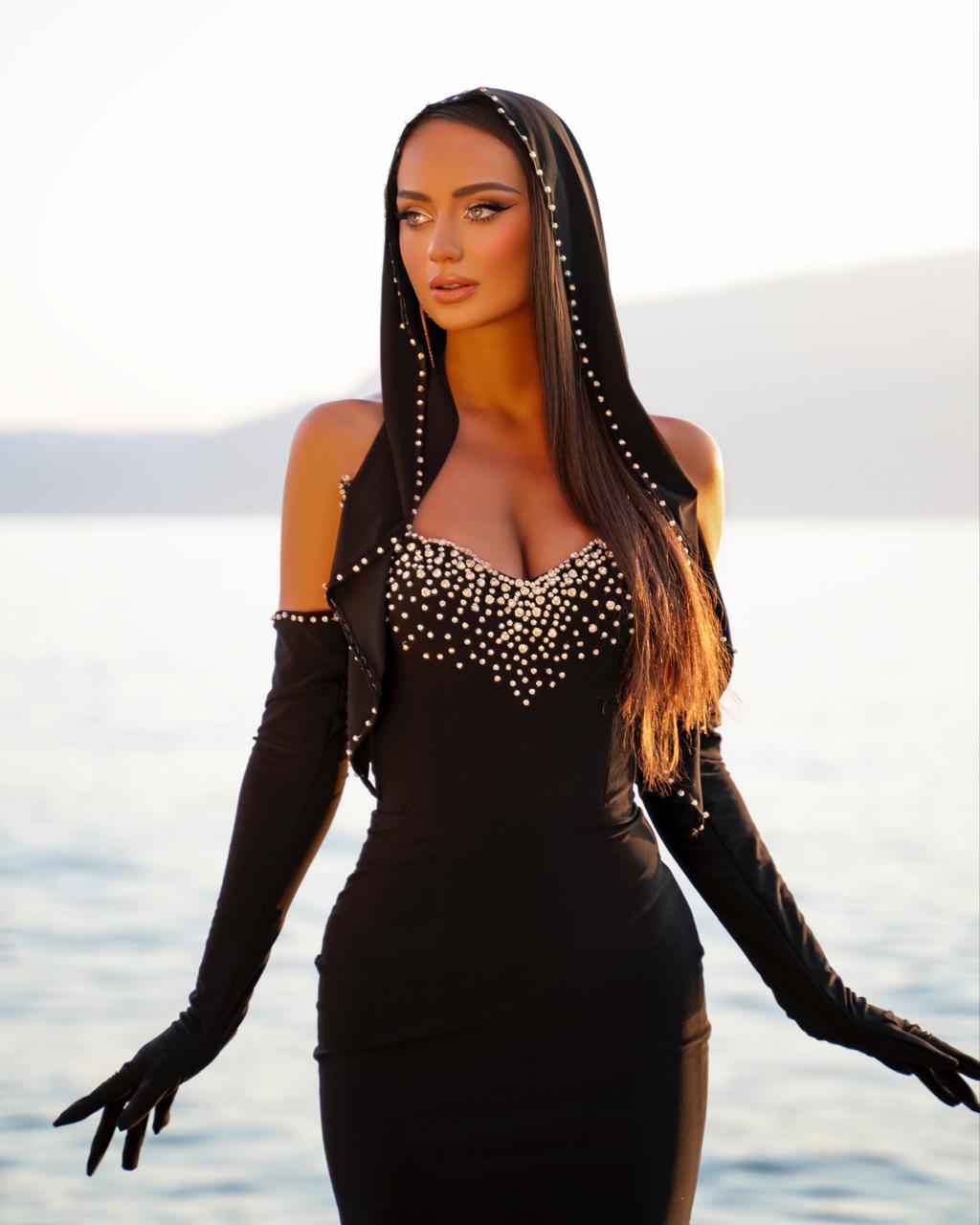 Woman in a black dress with studded details and long gloves by the water