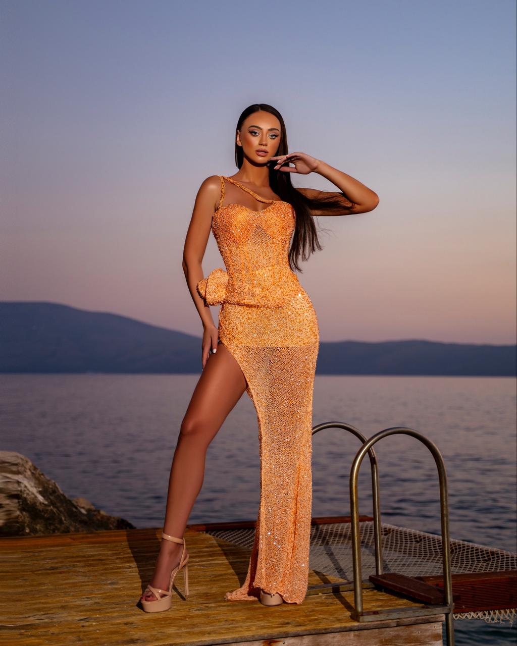 Woman in a sparkling orange dress standing on a dock with a scenic background