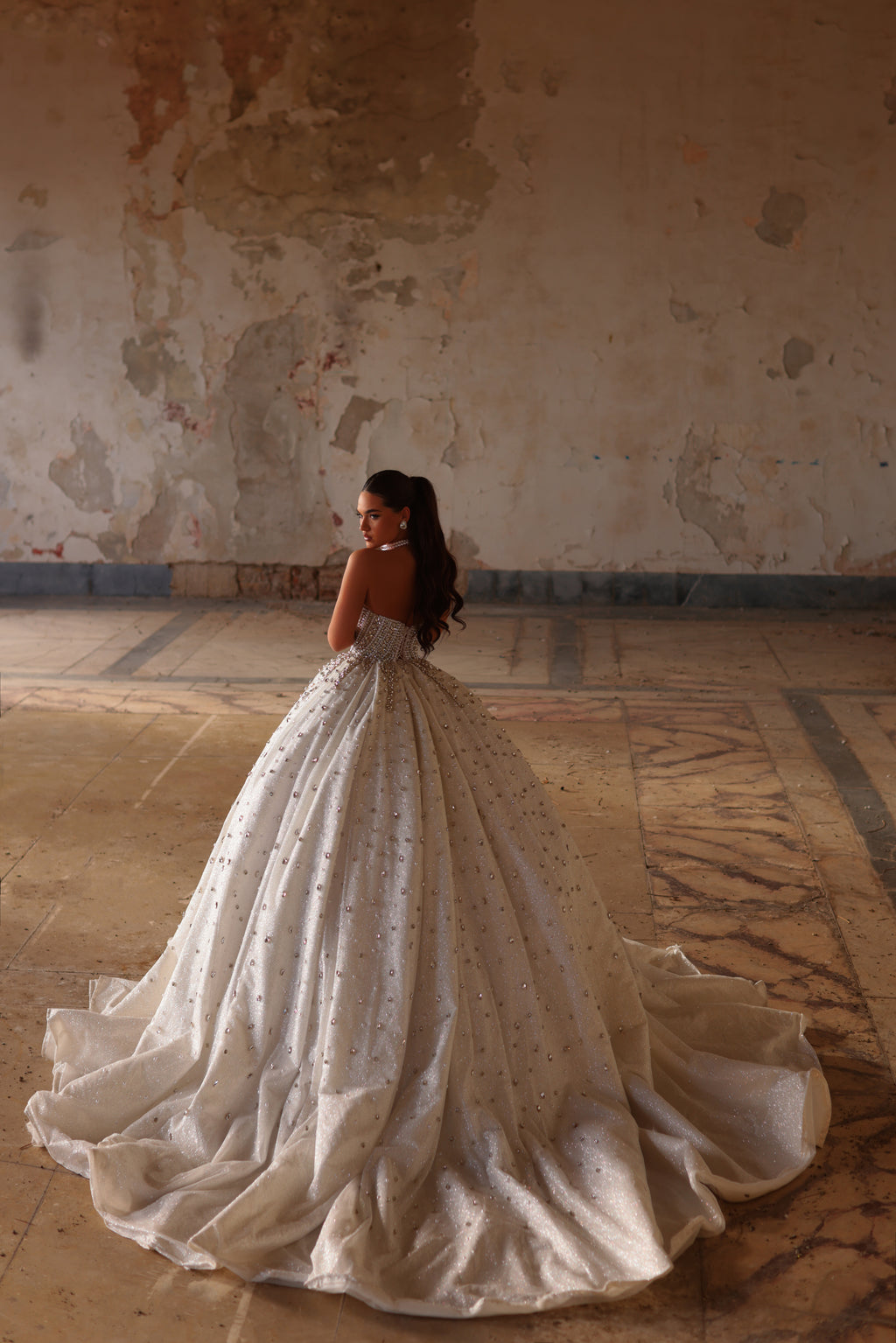 Woman in a white wedding dress standing in an old, textured room.