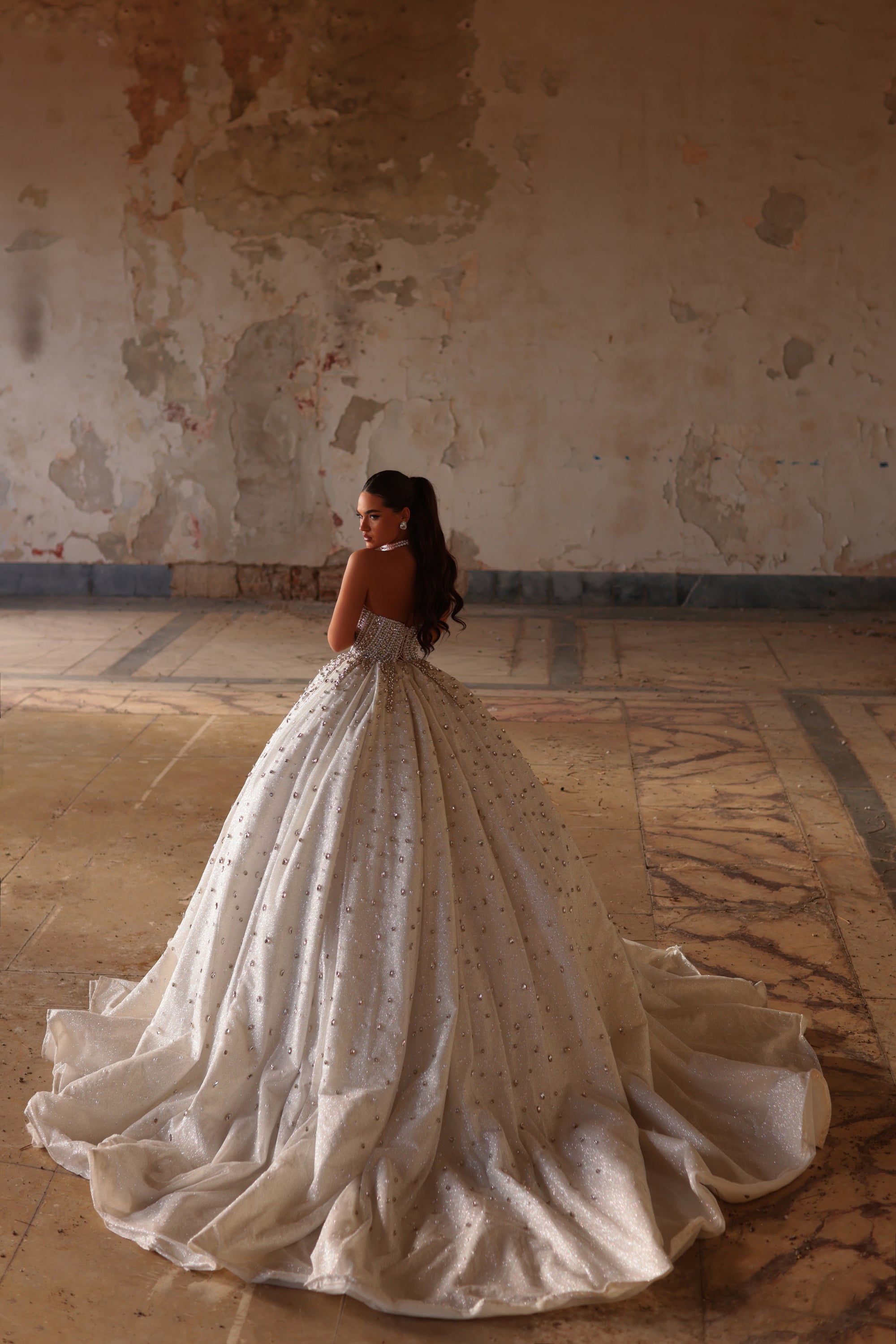 Woman in a white wedding dress standing in an old, textured room.