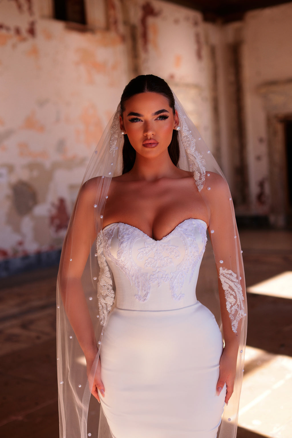 Woman in a white wedding dress with a long veil standing in an old building.