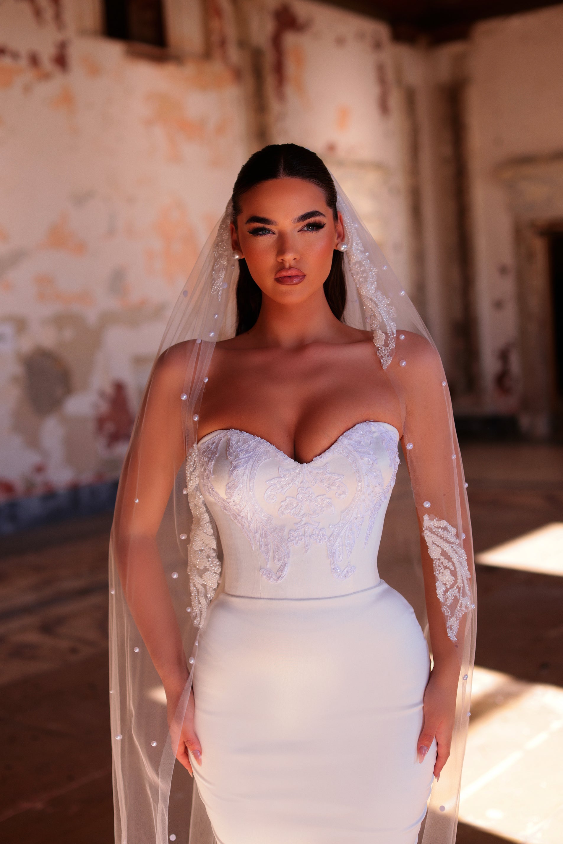 Woman in a white wedding dress with a long veil standing in an old building.
