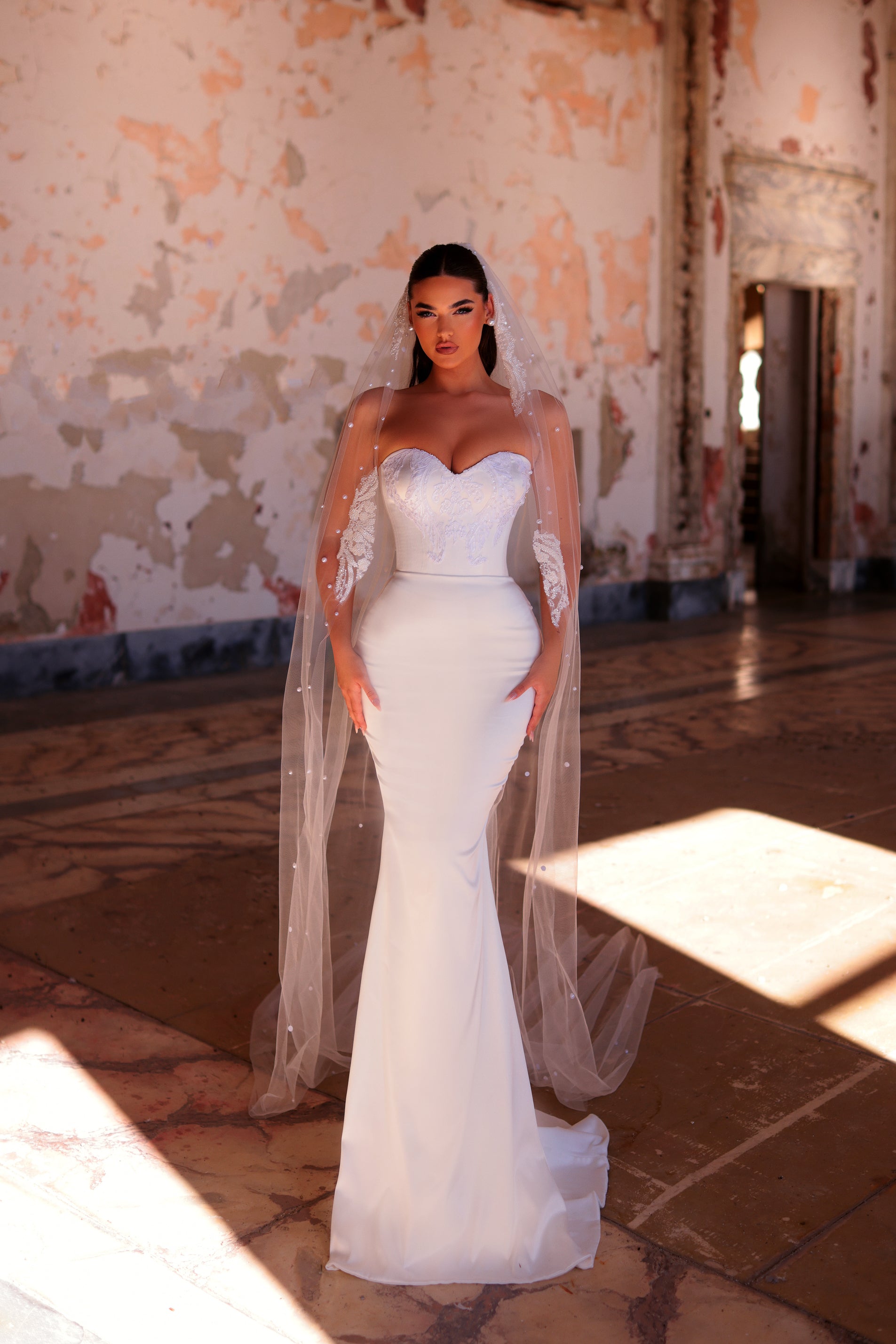 Woman in a white wedding dress with sheer sleeves standing in an ornate room.