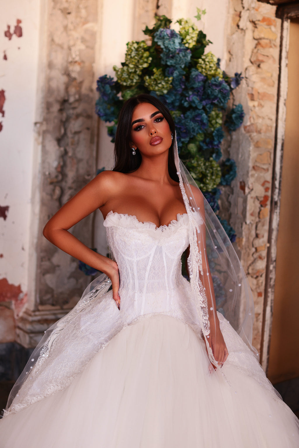 Woman in a white wedding dress with a veil standing against a decorative wall.