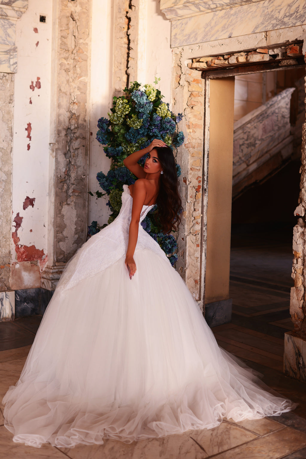 Woman in a white wedding dress holding a bouquet in an ornate room.