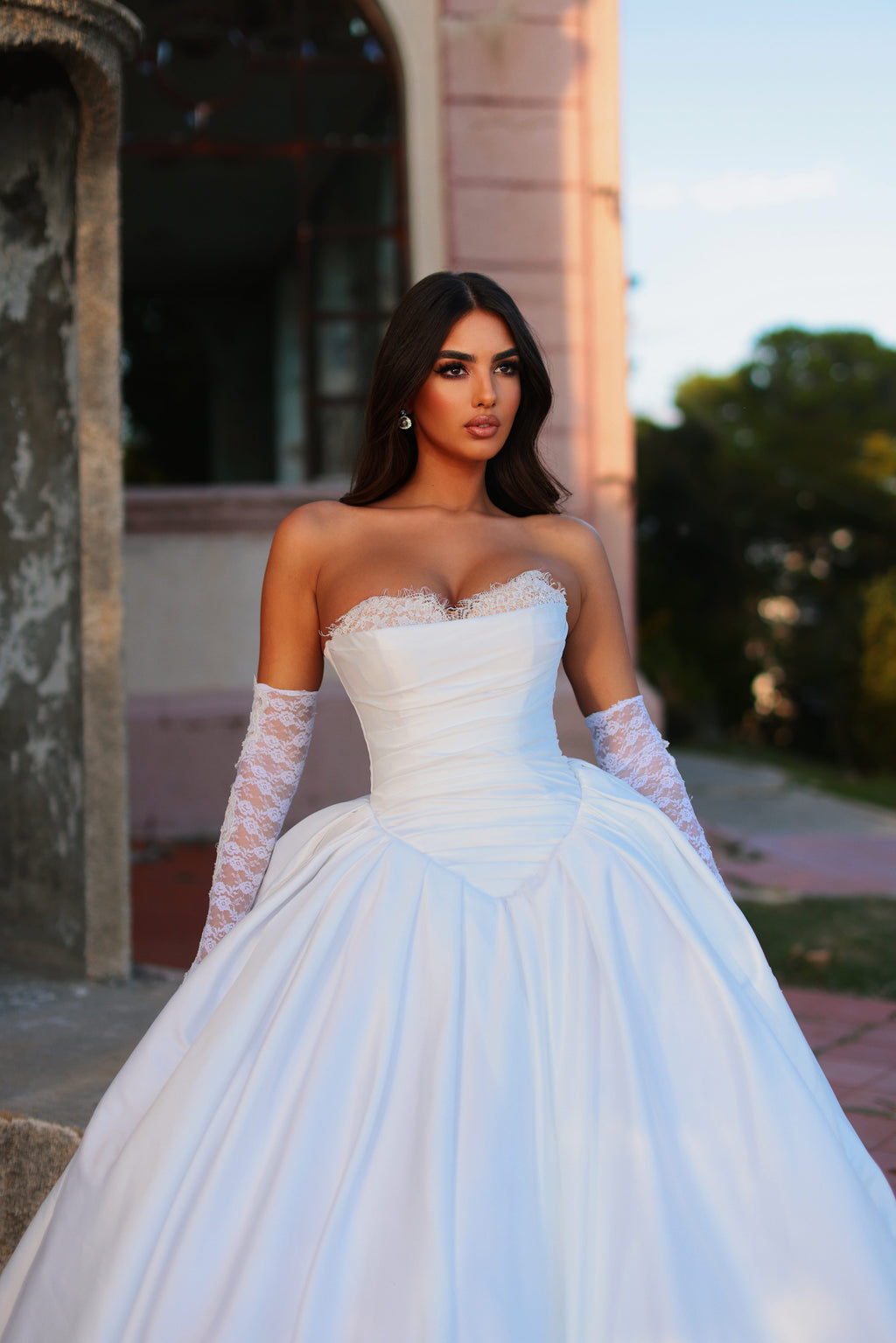 Woman in a white wedding dress with lace sleeves standing outdoors.