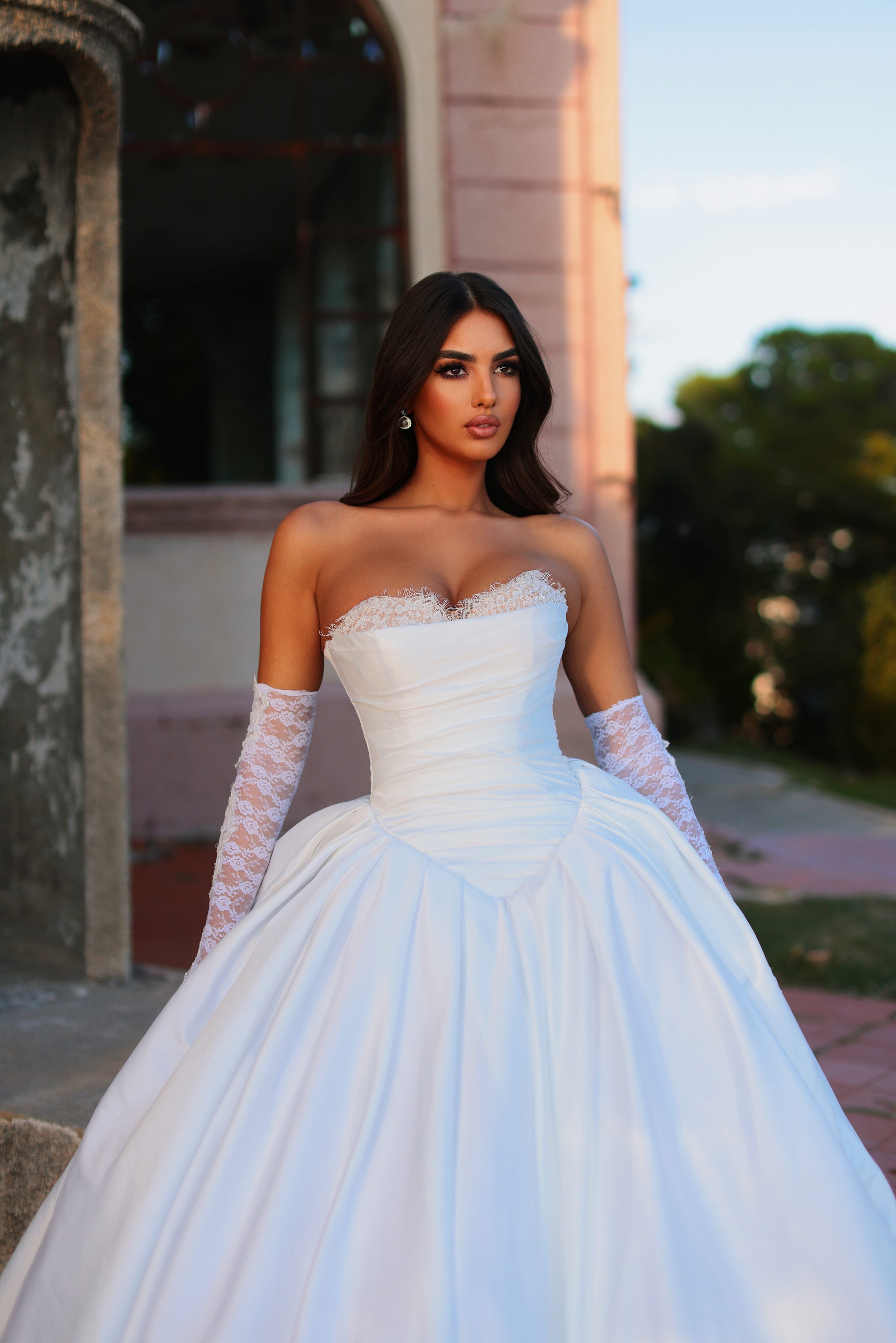 Woman in a white wedding dress with lace sleeves standing outdoors.