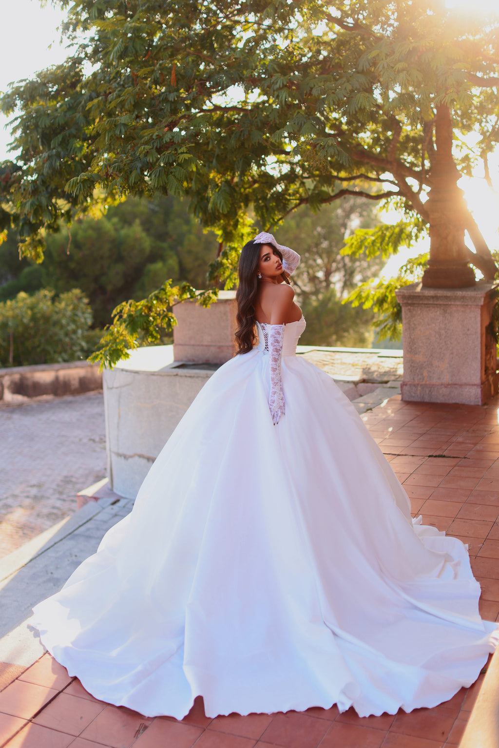 Woman in a white wedding dress standing outdoors with greenery in the background