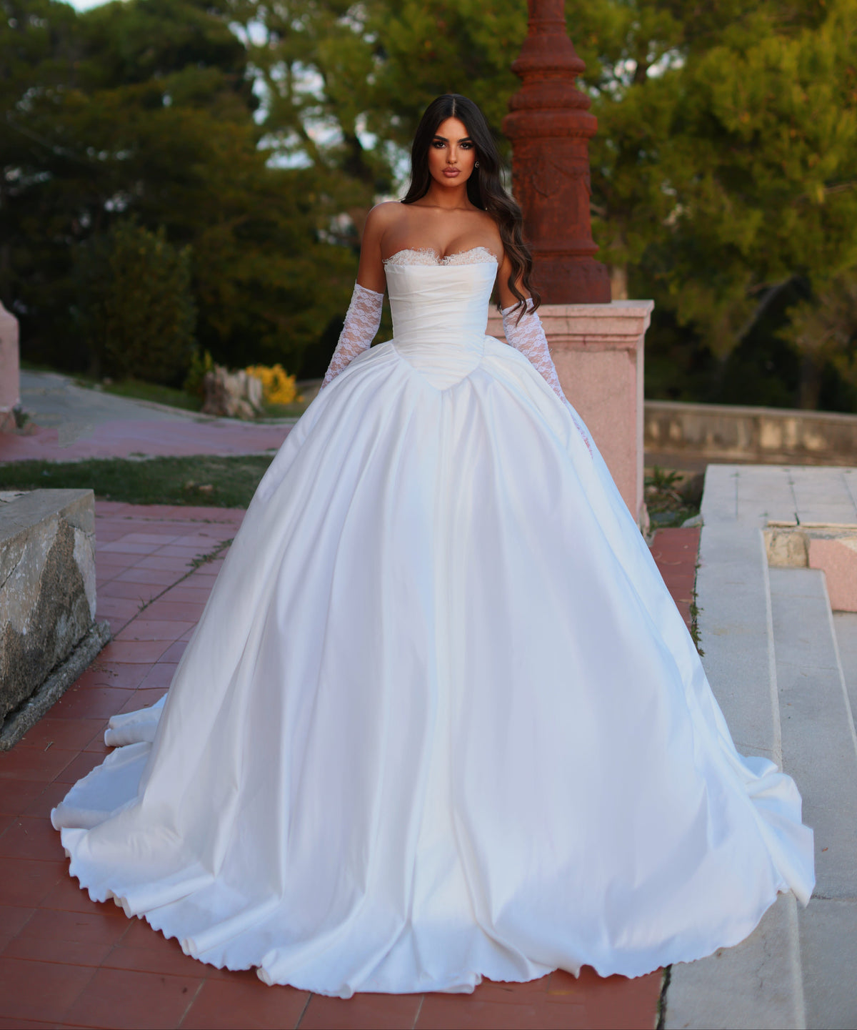 Woman in a white wedding dress standing outdoors with greenery in the background