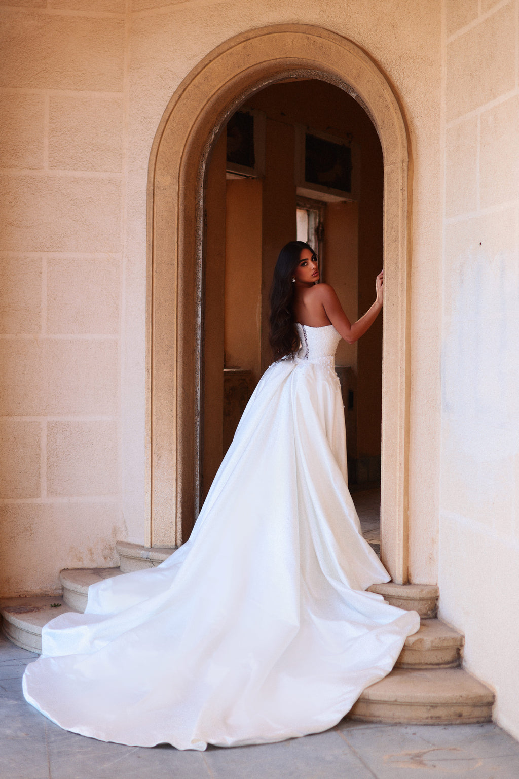 Woman in a white wedding dress standing in an archway of a classical building.
