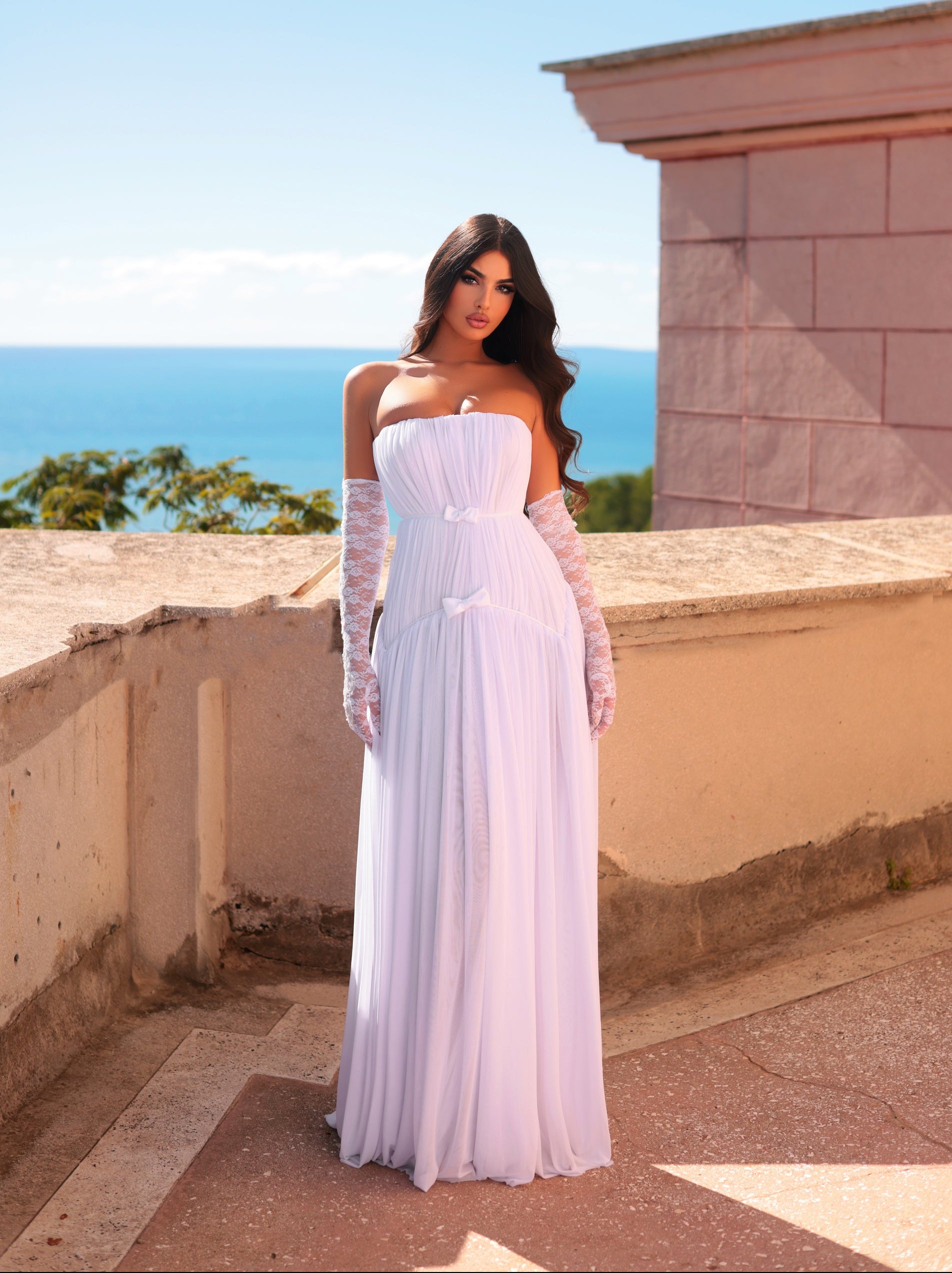 Woman in a white dress standing on a rooftop with ocean view