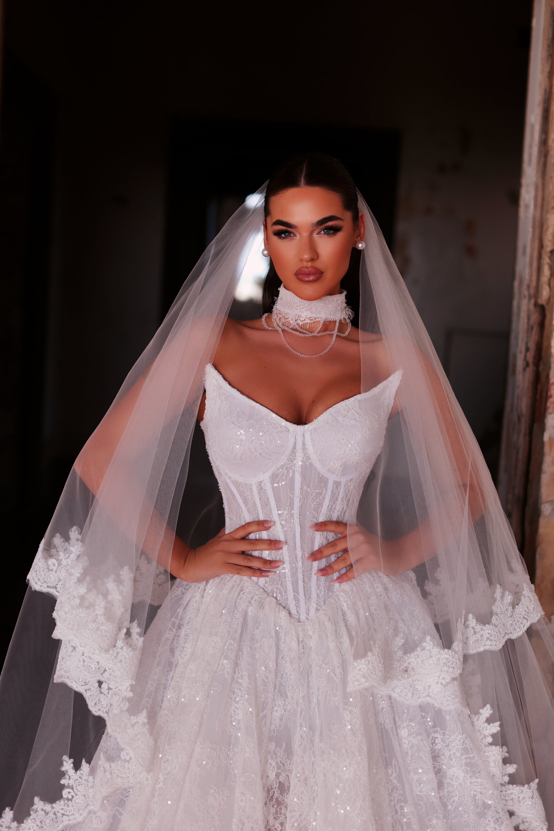 Woman wearing a white wedding dress with a long veil indoors.