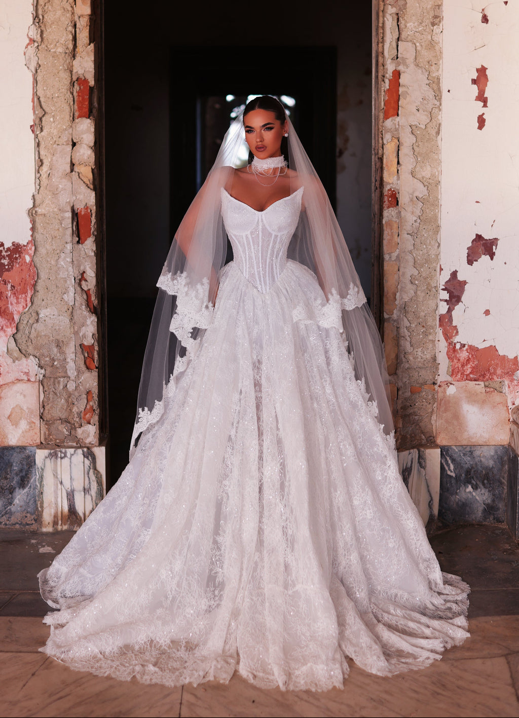 Woman in a white wedding dress with a long veil standing in a doorway.