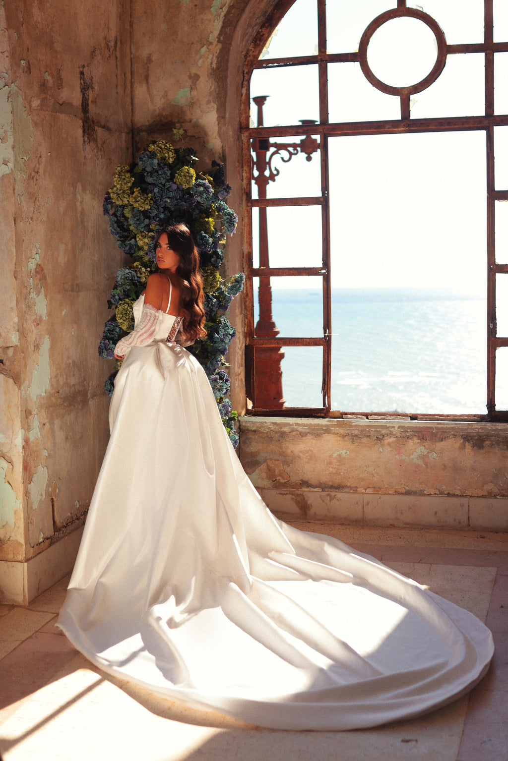 Woman in a white dress standing in a sunlit room with ocean view