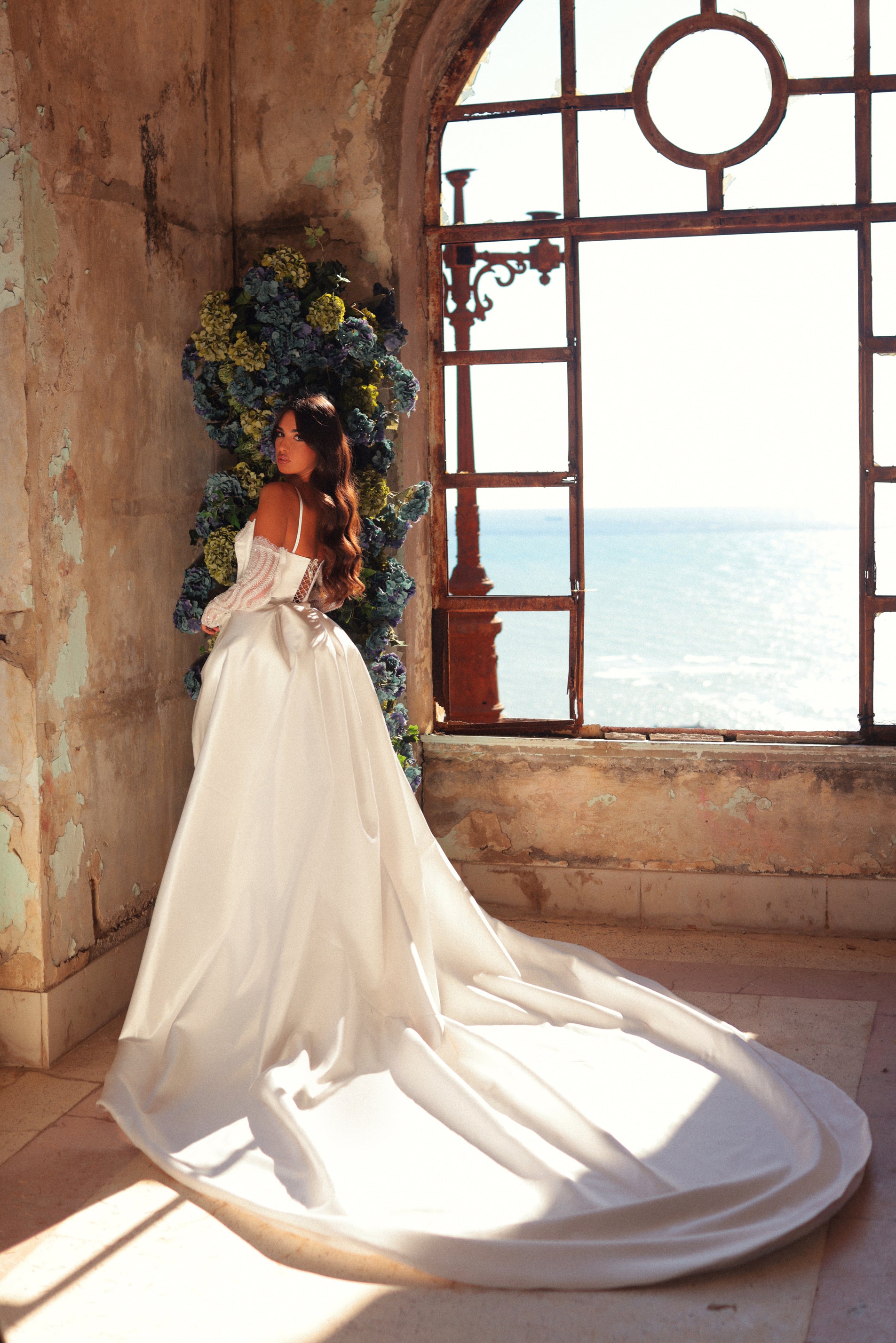 Woman in a white dress standing in a sunlit room with ocean view